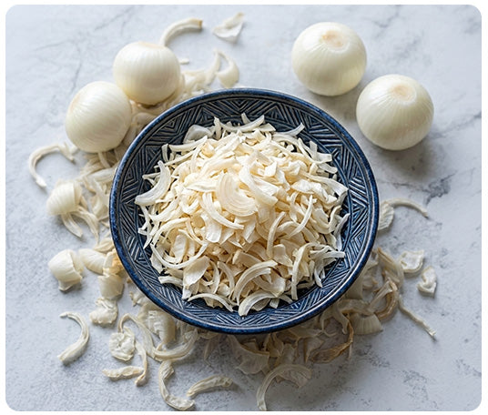 Bowl of premium dehydrated onion flakes surrounded by fresh onions and dried onion slices, showcasing Food and Faith's 100% single ingredient onion flakes for cooking, soups, gravies, and seasoning.
