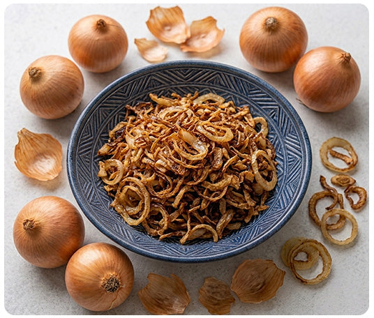 Bowl of premium fried onions surrounded by fresh brown onions, ideal for biryani, curries, gravies, and everyday cooking with rich flavor and ready to use convenience.

